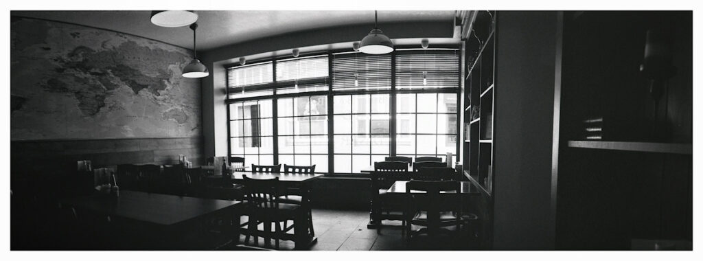 Black and white panoramic photograph of the interior of a cafe