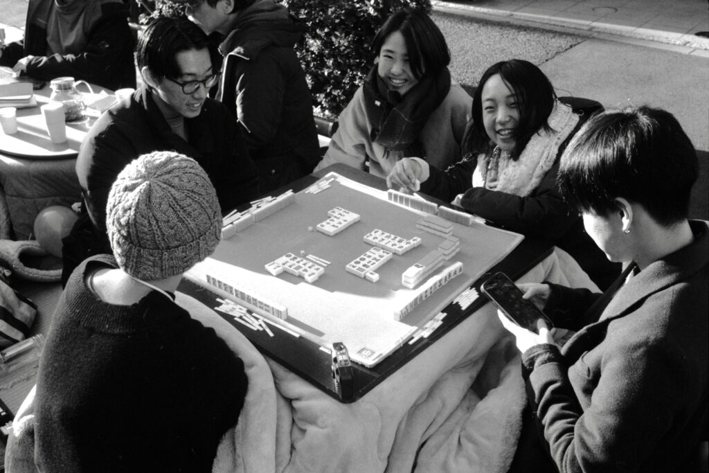 Group of kids playing a mahjong outdoors in a kotatsu.Shot on Nikon S3 Olympic with 35mm W-Nikkor f/3.5 lens, on Kentmere 400 