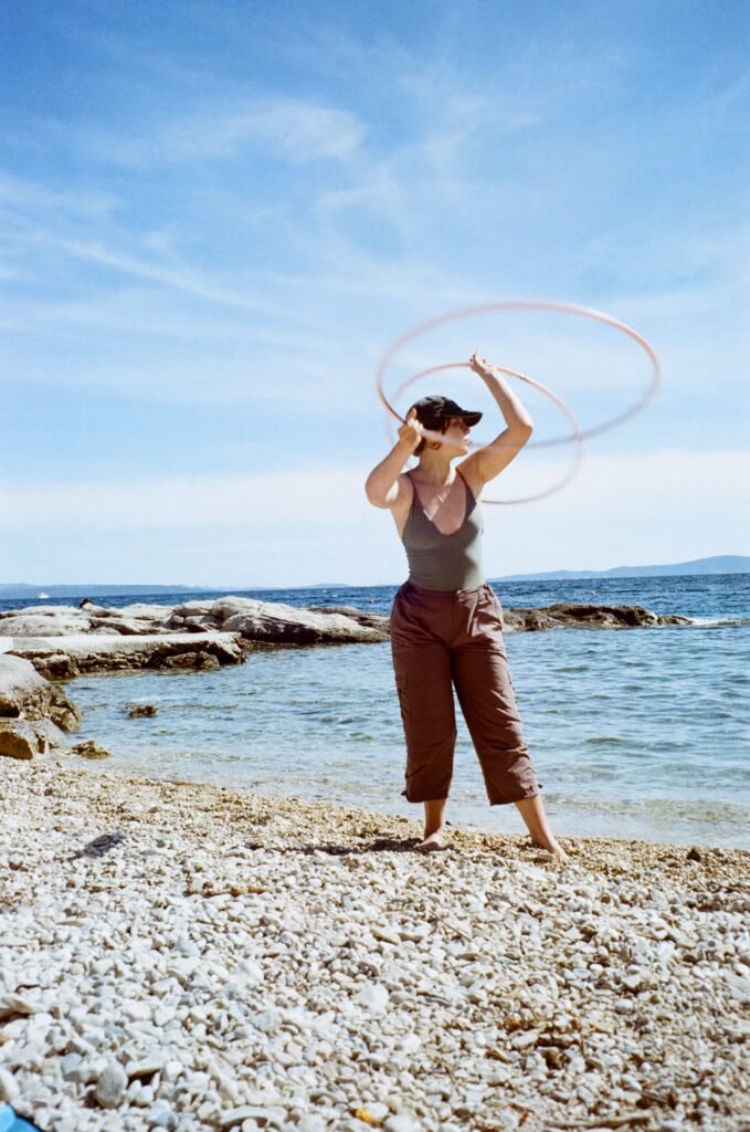 A young woman spinning two hula hoops on a beach.