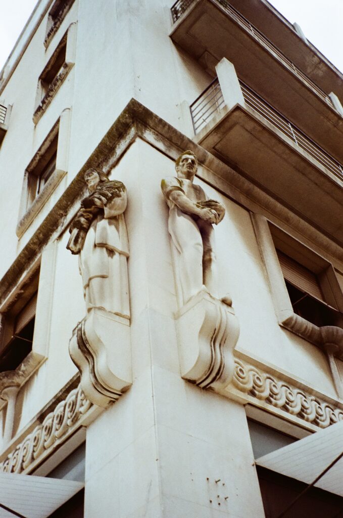 The corner of a tall stone building. Two stone figures carved into either side.