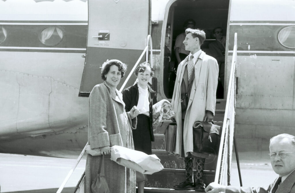 A black-and-white photo of a woman, girl, and teenage boy on the steps of an old airplane.