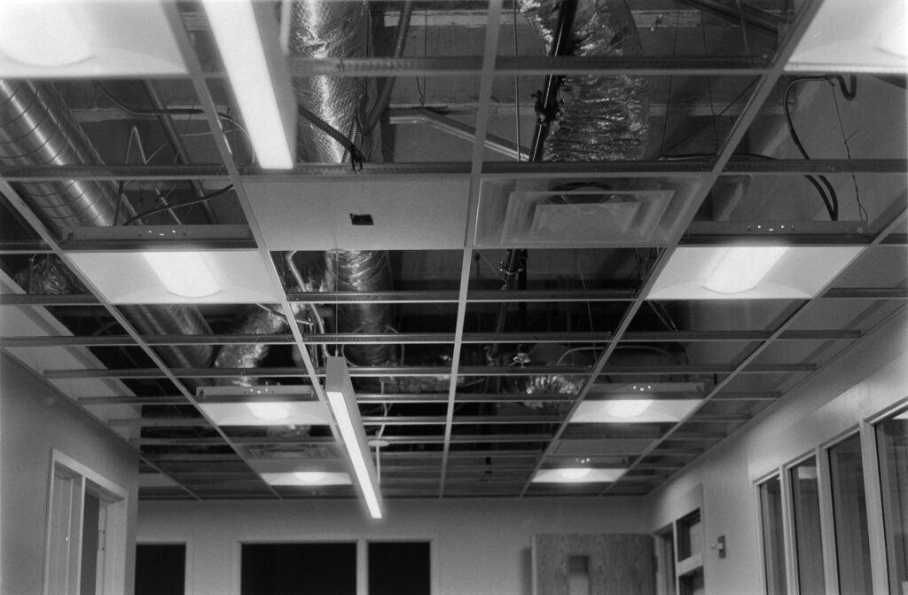 Black and white image of an open ceiling grid shows exposed HVAC and electrical work