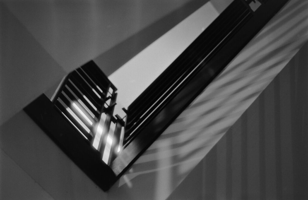 Black and white image looking upward threw a stair way, the light causing drastic shadow across the white drywall