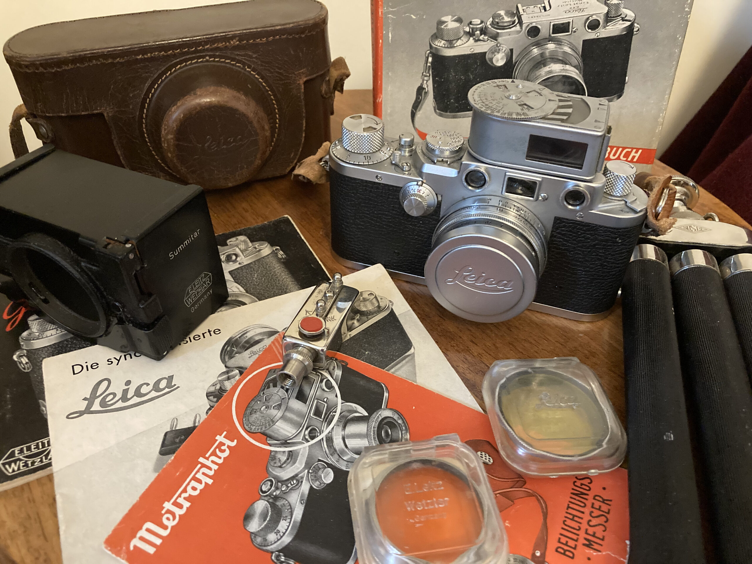 A Leica IIIF camera with lens, leather case, yellow and orange lens filters, self-timer, tripod, and lens hood and associated Leica manuals.