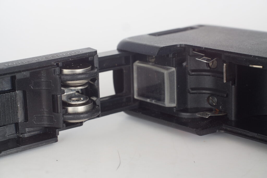 Both sides of the battery contacts - in door and in the camera body. Making contact only when door is closed.