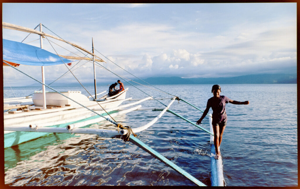 A girl balancing on the outrigger of a boat.