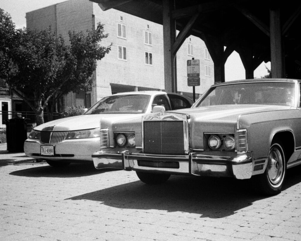 Two large american sedans, one from the 90s, one from the 70s, parked next to each other