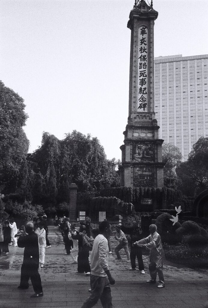 A group of people exercising below a tall, thin tower.