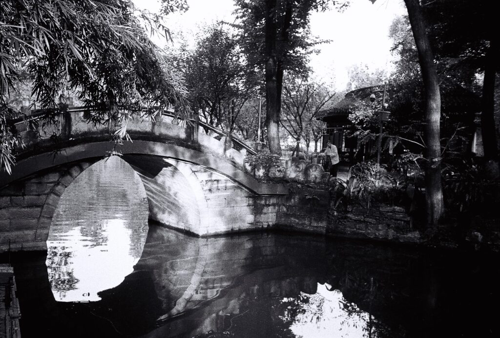 A curved Chinese style bridge over a stretch of water.