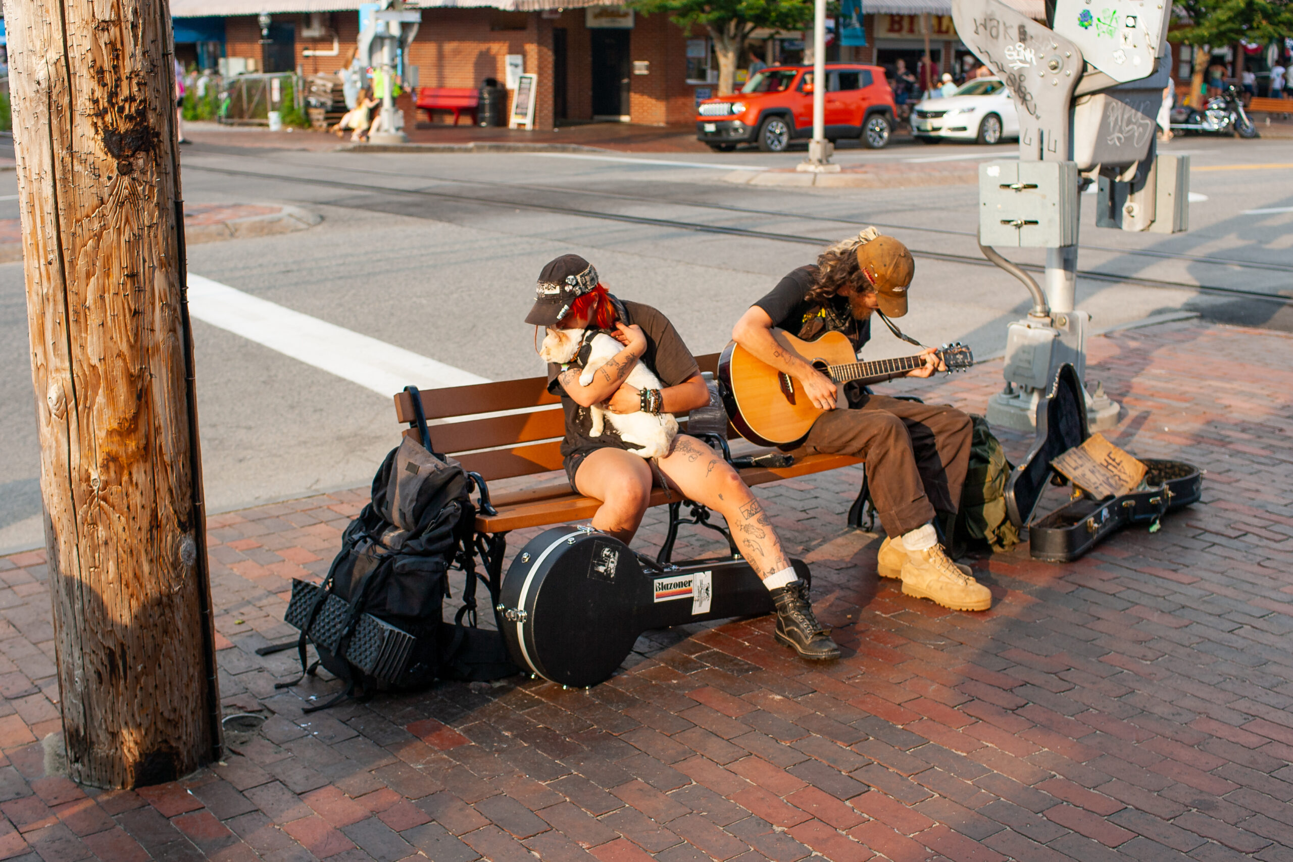 Two people, one holding a guitar. One kissing her cat which she is holding tightly on a bench.