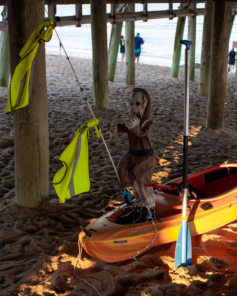 Large Doll, grey face with black eyes, strapped to kayak 