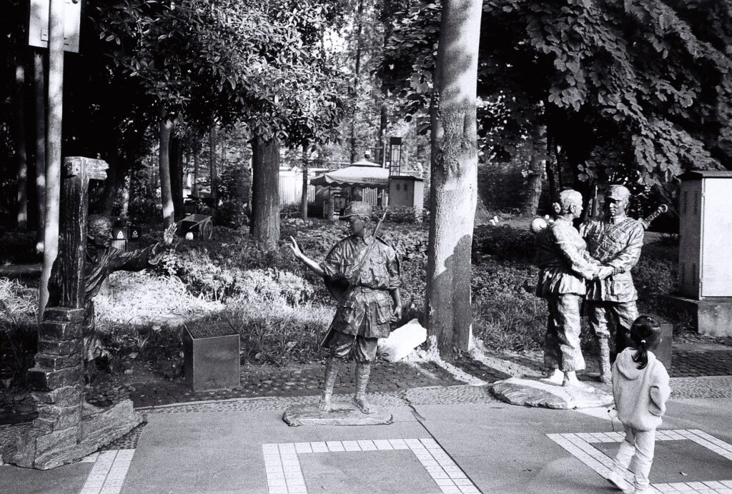 A girl looking at 3 statues representing military figures.