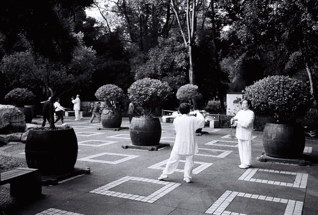 Two women wearing white engaged in mock ritual swordplay.