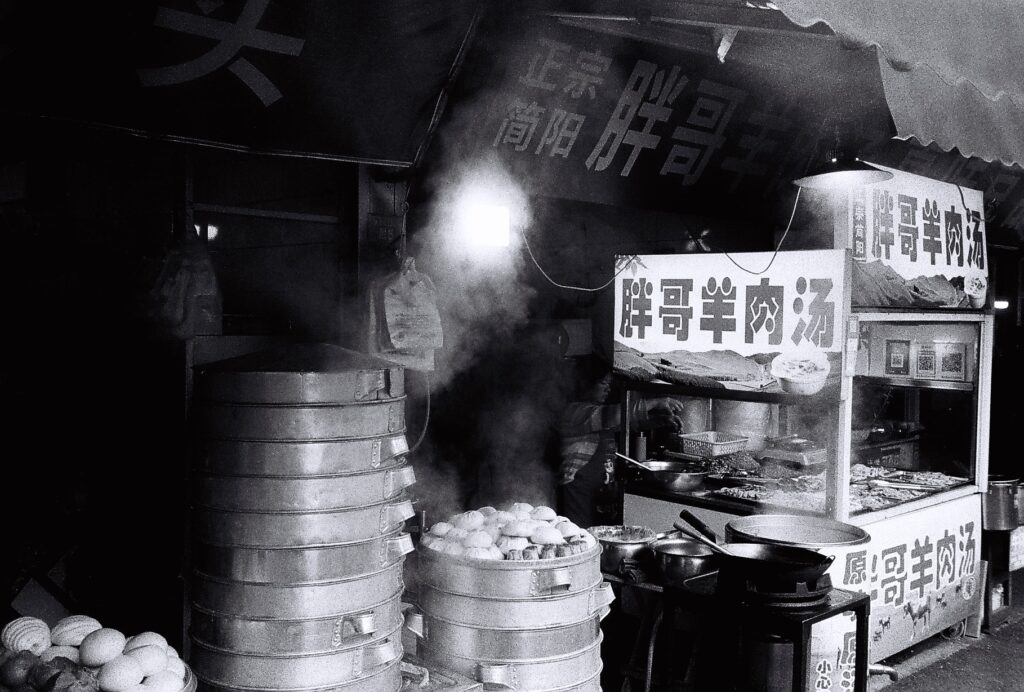 food vendors stall alongside silver containers which are steaming food.