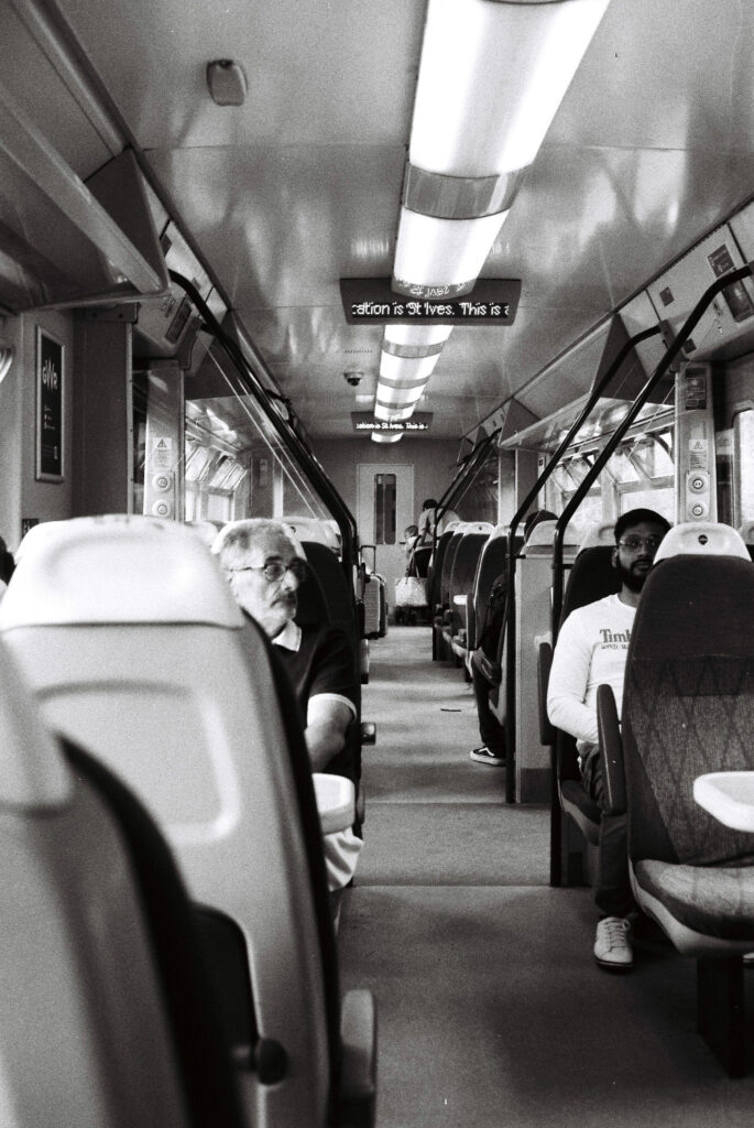 Black and white photo of two passengers looking at each other from opposite sides of the train aisle.