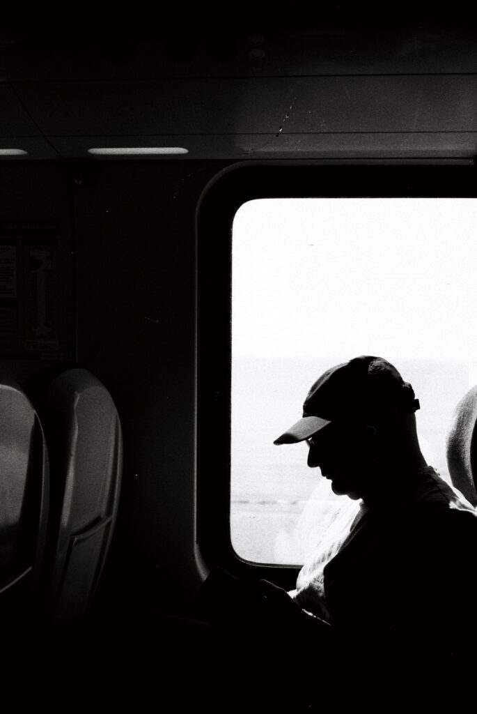 Black and white photo of a person, side-profile, silhouetted in front of a train window.