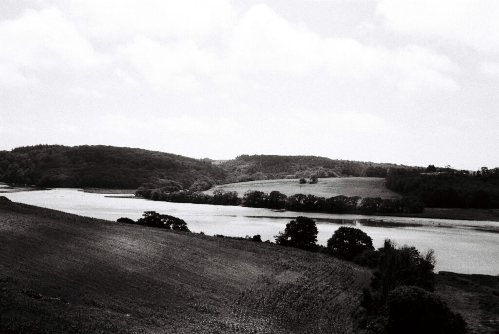 Black and white photo of hills and a river with trees.