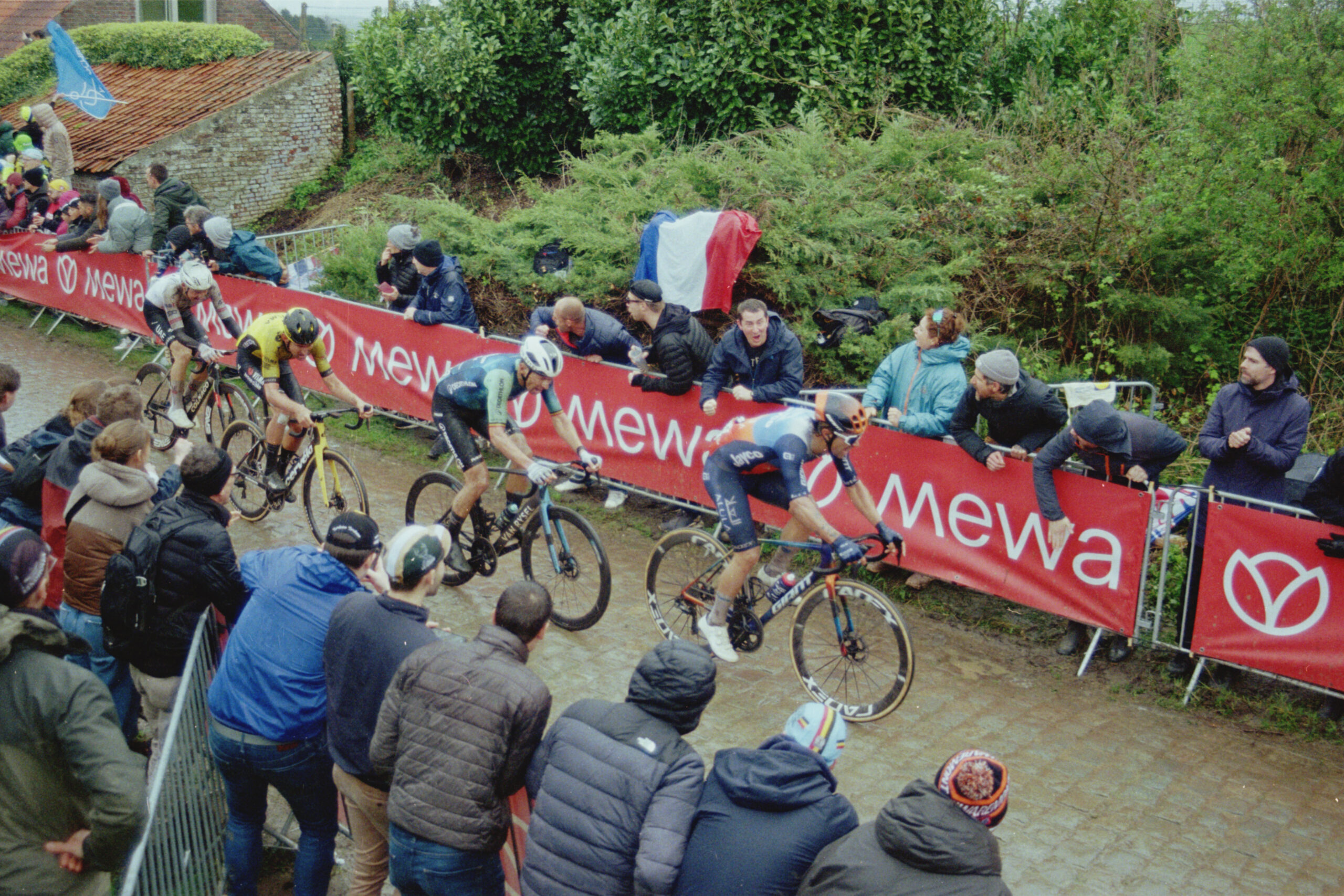 Four cyclists ride along a cobbled street while fans cheer them on during the 2024 Tour of Flanders