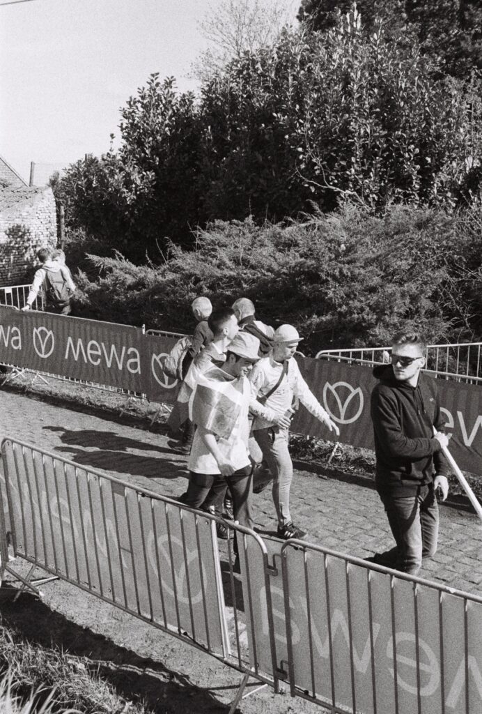 Four men, one with a Basque flag wrapped around his shoulders, walk along a cobbled street hemmed in by barriers.