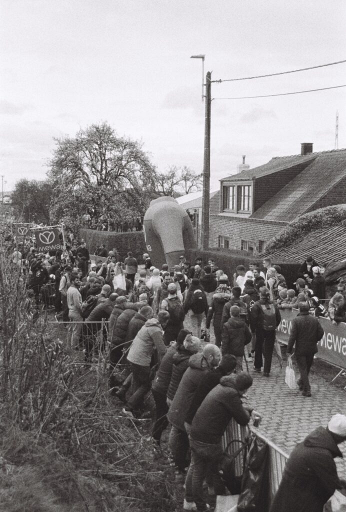 A group of fans walk along a cobbled street while others line the barriers at the side of the street.