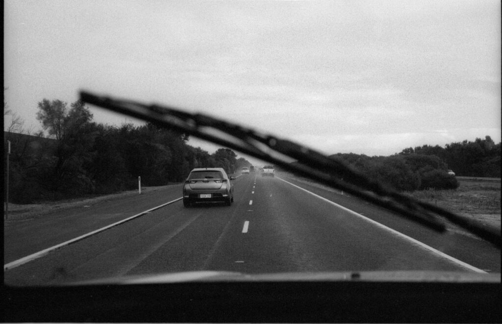 Cars on the highway, whilst it's raining, framed by the windscreen wiper