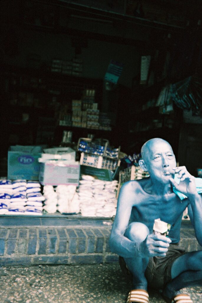 Man sitting on a sidewalk smoking a cigarette