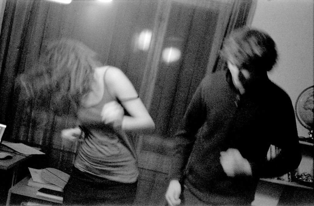 A blurry black and white photograph of a woman and a man dancing at a house party.