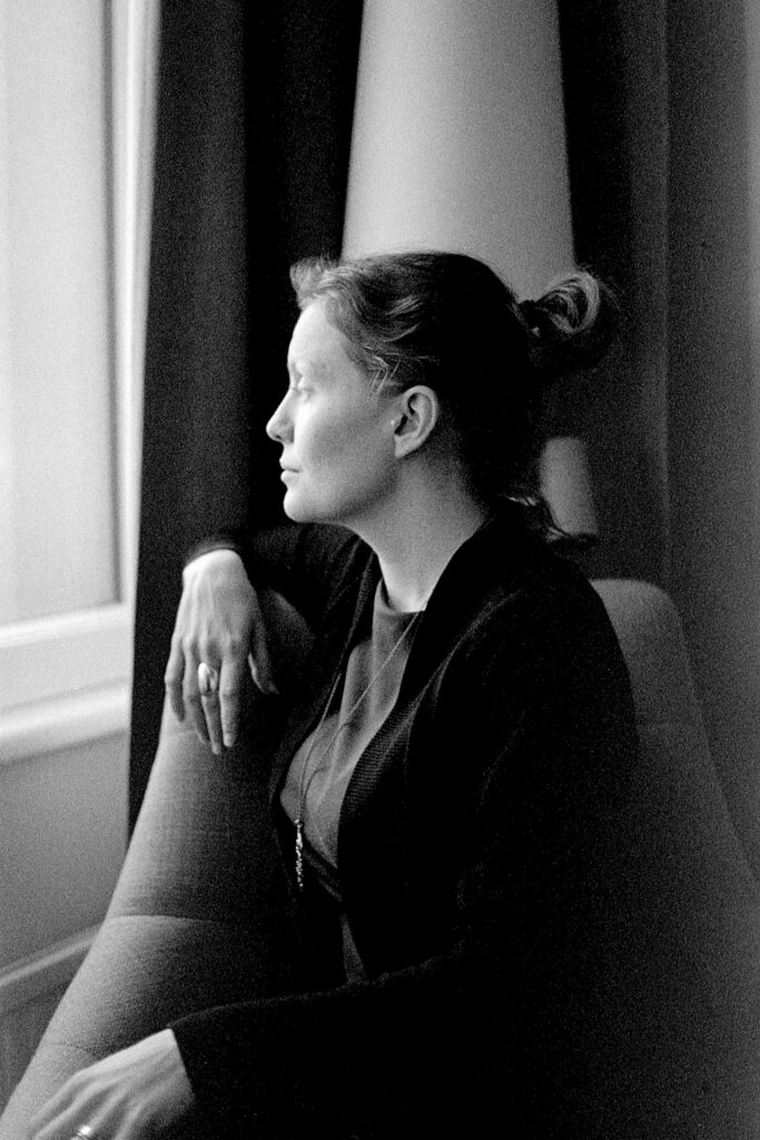 A black and white photograph of a woman's profile. She's sitting in an armchair. She's looking out of the window. 