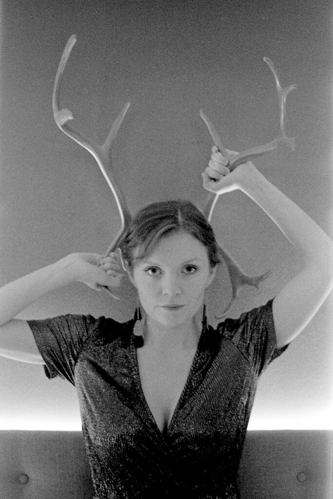 A black and white photograph of a woman in a dress holding reindeer antlers on her head.