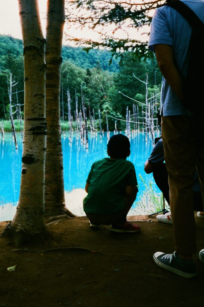 A child squats in front of an electric blue pond.