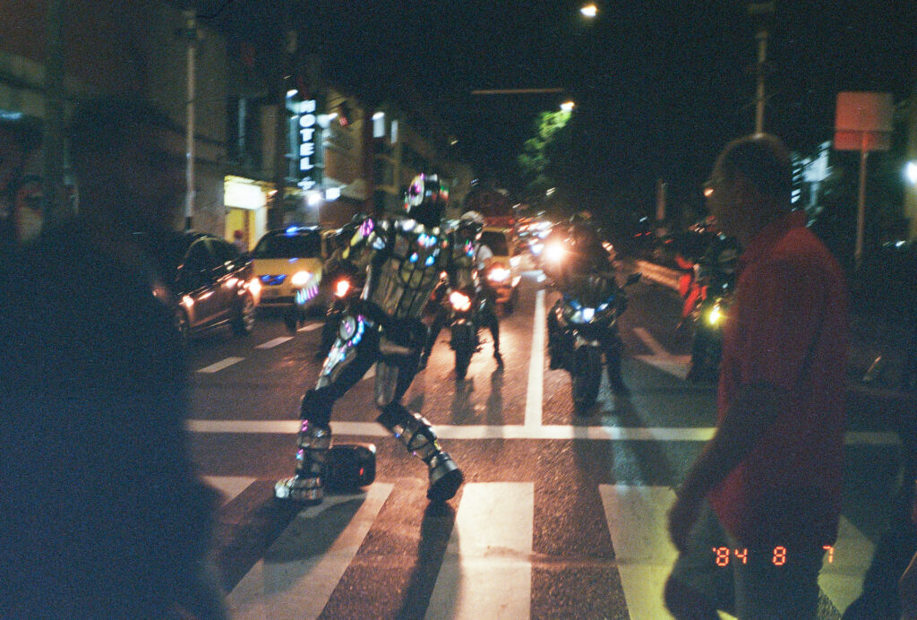 Color photograph of street dancer in robotic outfit in front of traffic