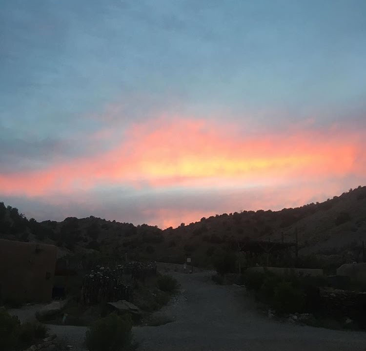 a blue, pink, and yellow sky with a hint of a sun dropped below horizon, in a hilly, rocky desert landscape