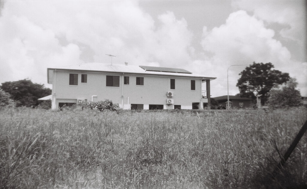 A field of unkempt grass, with a townhouse on the plot next to it